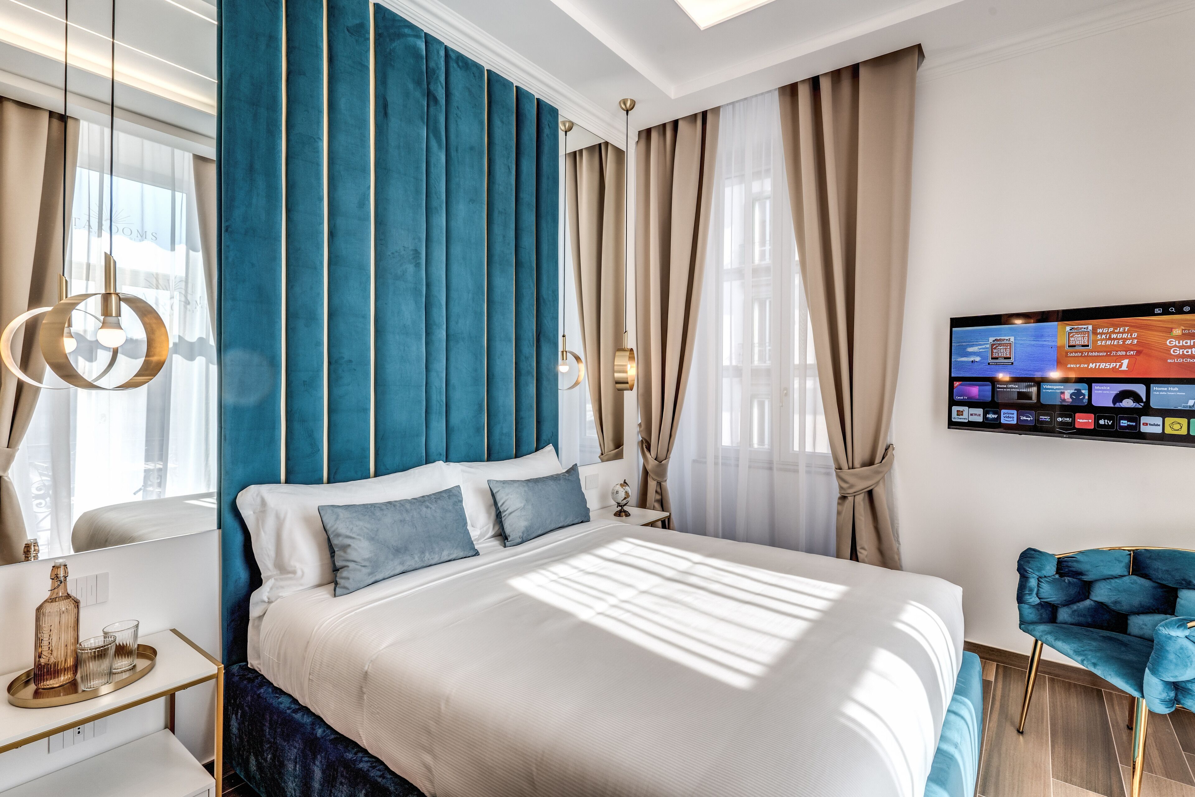 Une chambre d’hôtel moderne avec un grand lit, un téléviseur fixé au mur et une chaise bleue.
