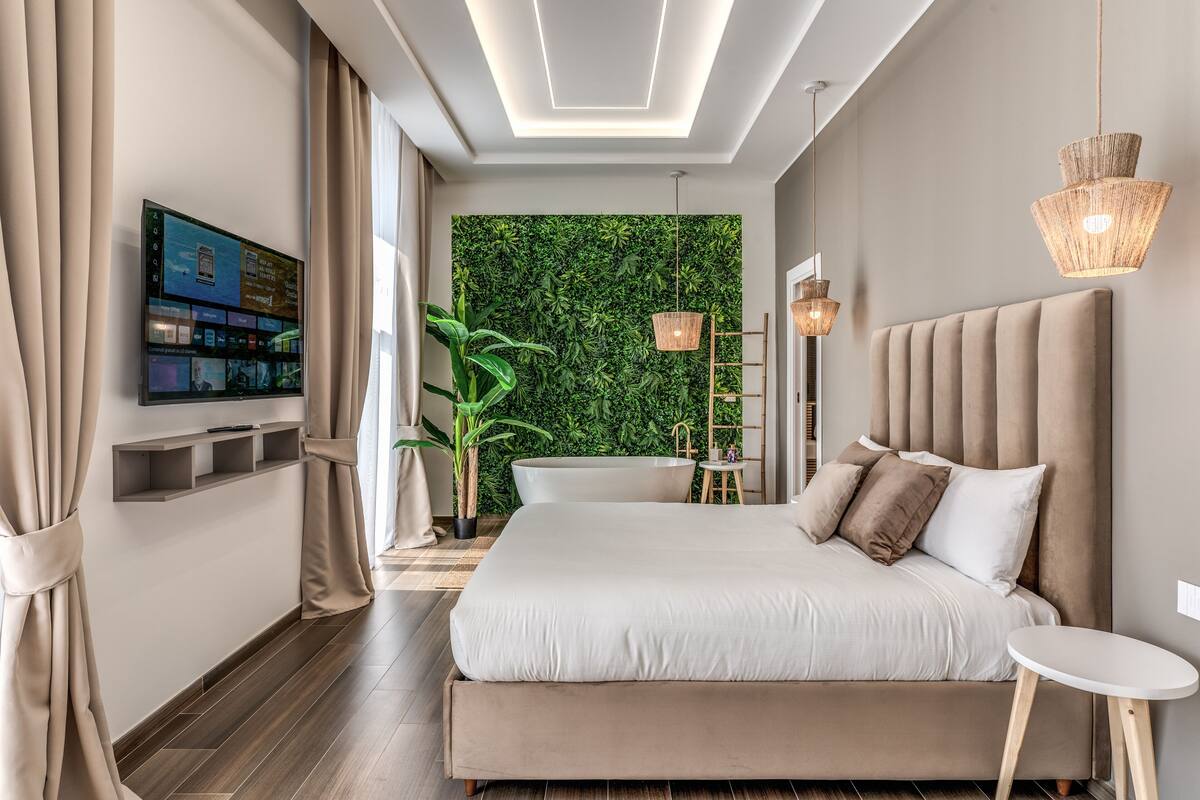 A modern bedroom with a large bed, a TV mounted on the wall, and a green wall feature.