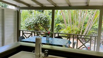 A covered outdoor kitchen area with a sink and a table, surrounded by lush greenery.
