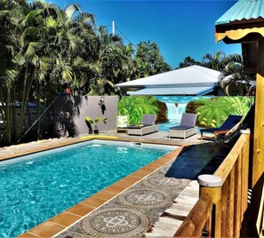 A swimming pool with lounge chairs, a waterfall feature, and tropical vegetation. - Gîte Lagon - Baz Créole (Deshaies)