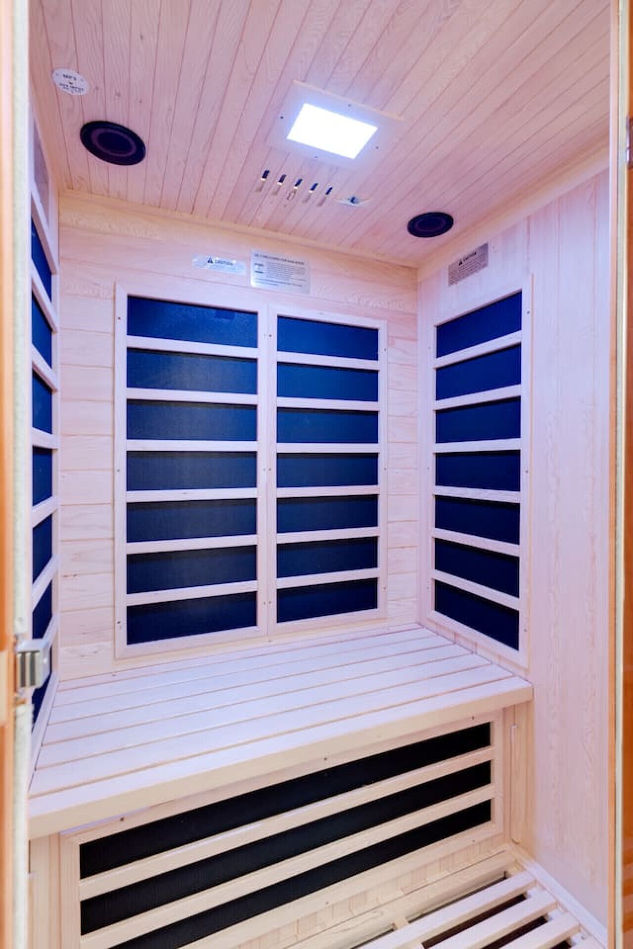 Una sauna con paredes y bancos de madera, una luz en el techo y rejillas de ventilación.