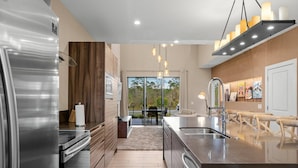 Une cuisine moderne dotée d’appareils électroménagers en acier inoxydable, d’un grand îlot central avec un évier et donnant sur une terrasse extérieure.