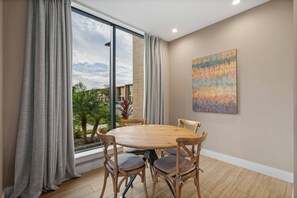 Un comedor con una mesa redonda y sillas, ventanas amplias con cortinas y un cuadro en la pared.