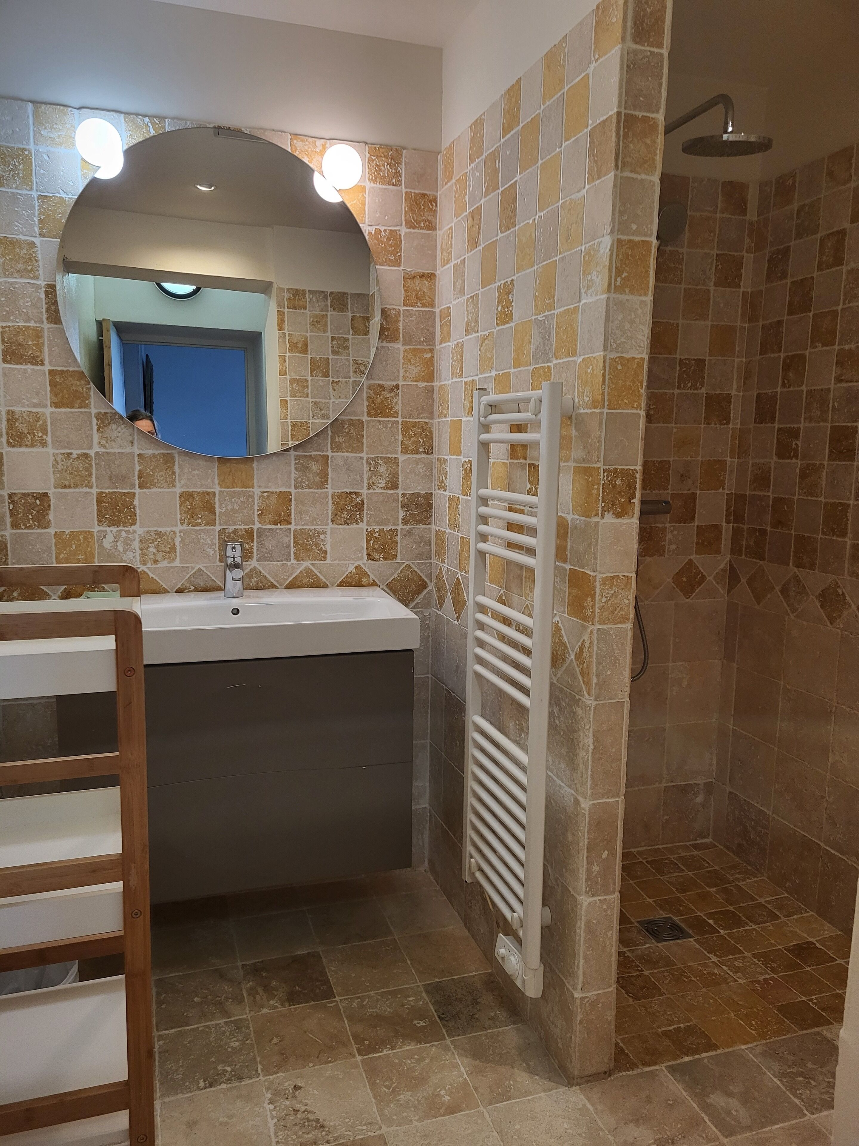 A bathroom with a sink, mirror, shower, and tiled walls.