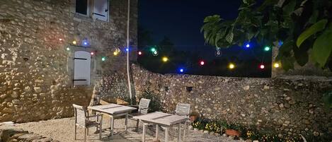 Un área de estar al aire libre con muros de piedra y suelo de grava, decorada con luces de colores.
