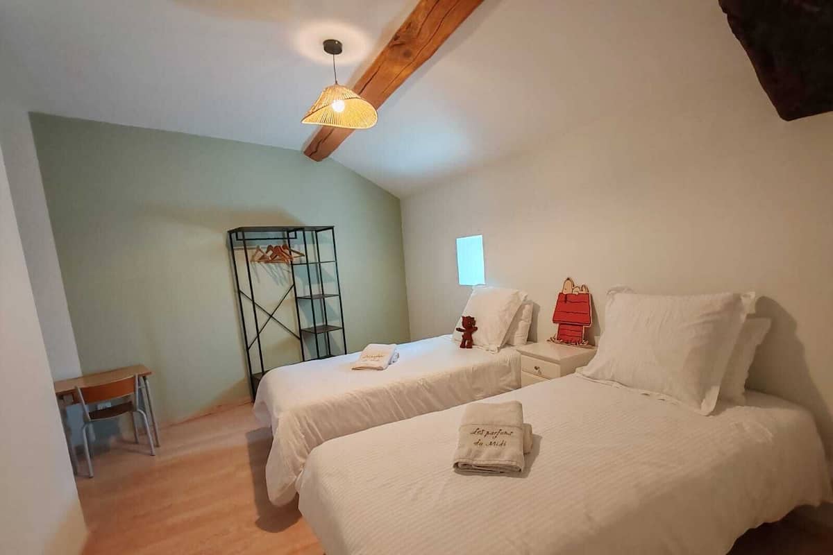 Un dormitorio con dos camas, un escritorio, una silla, una lámpara colgante y una ventana pequeña.
