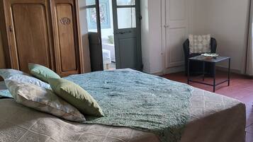 Quarto com uma cama grande, um guarda-roupa de madeira, uma mesa pequena com um prato e uma cadeira.