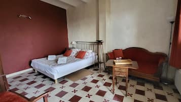 Un dormitorio con cama, una mesita, una silla y un sofá rojo.