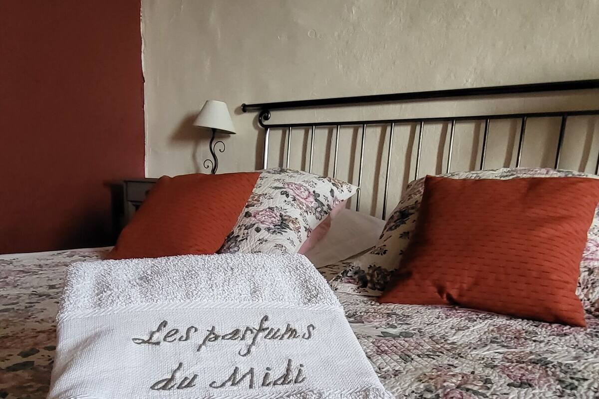 Una cama con colcha floral, una toalla blanca con texto y dos almohadas anaranjadas.