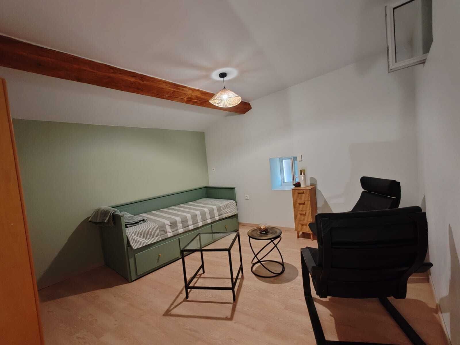 A small room with a bed, a desk, a chair, a small table, and a ceiling fan.
