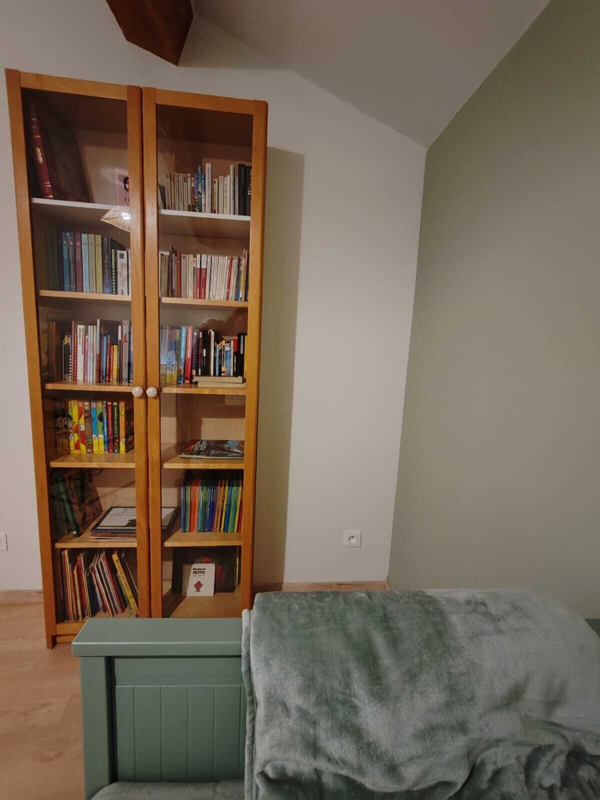 Une pièce avec une bibliothèque en bois remplie de livres, un banc recouvert d’un tissu vert et un radiateur.