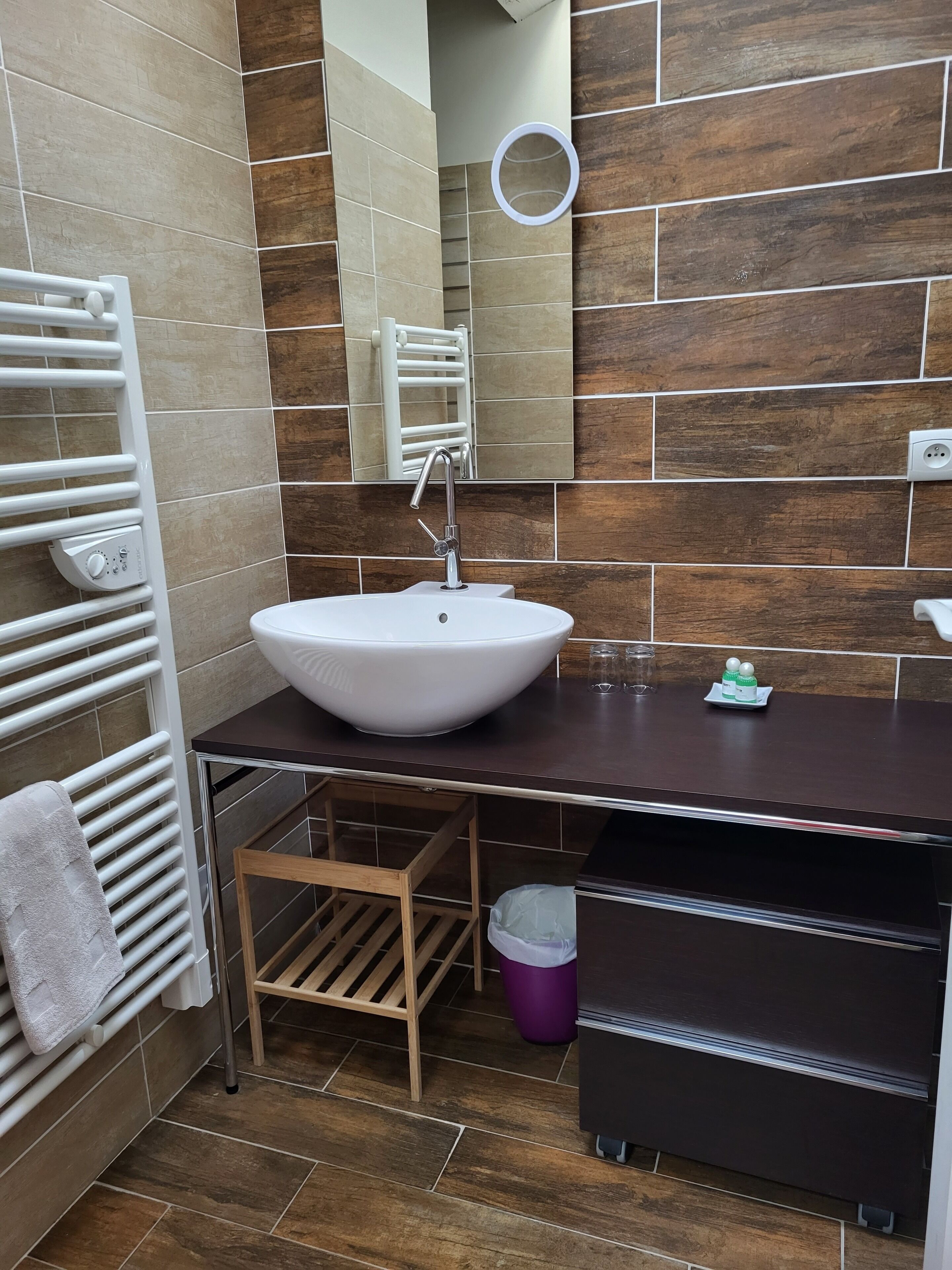 Une salle de bain avec un lavabo blanc, un miroir, un porte-serviettes et un petit tabouret en bois.