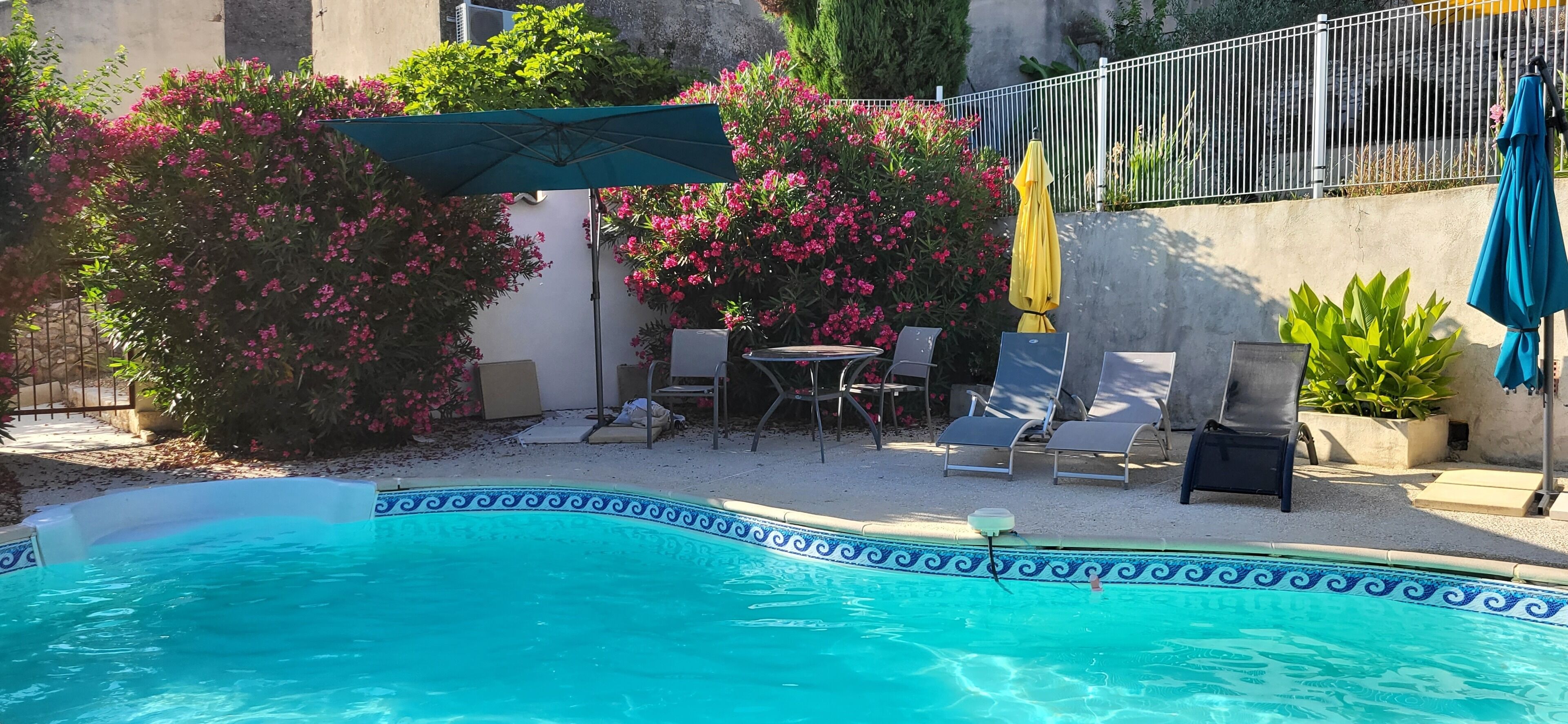 Una piscina con un borde decorativo, rodeada de sillas de descanso y una mesa.