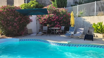 Una piscina con un borde decorativo, rodeada de sillas de descanso y una mesa.