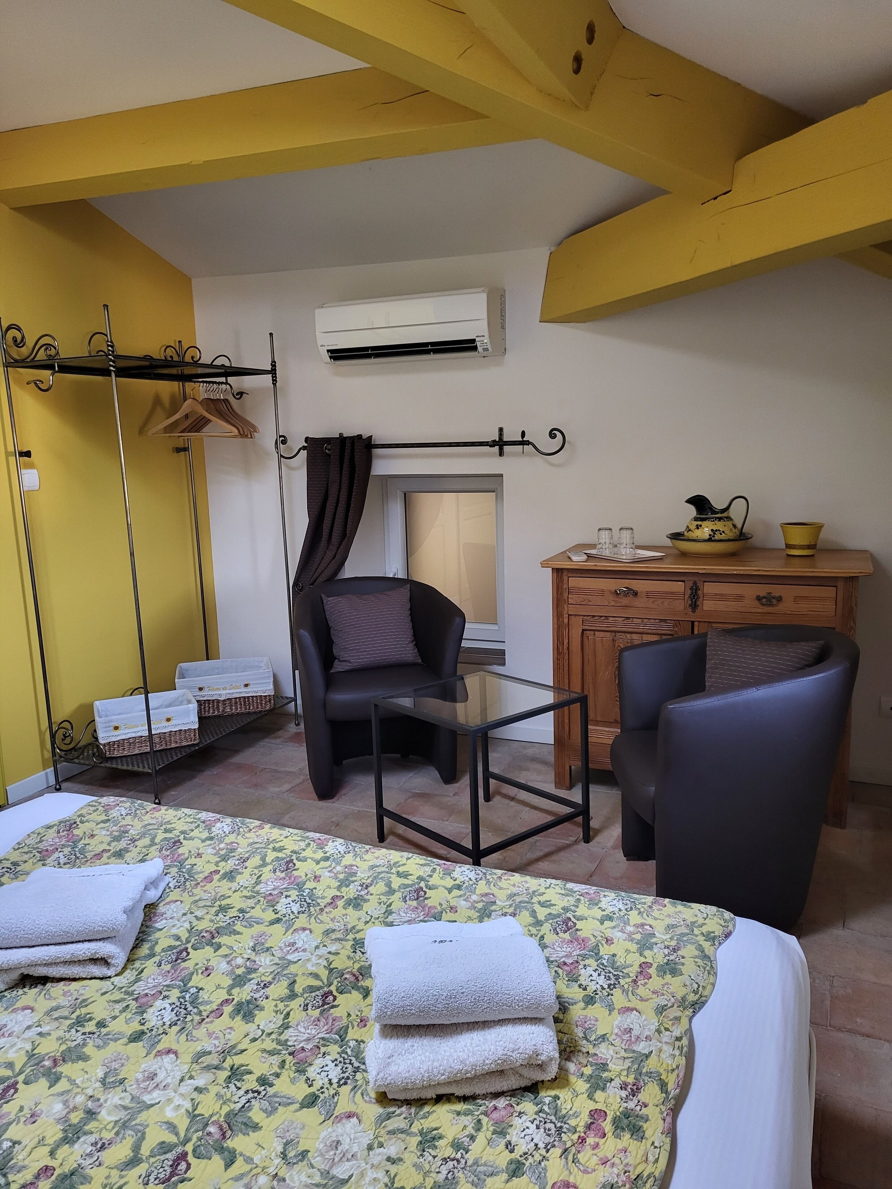 A room with a bed, two chairs, a small table, a dresser, and a hanging clothes rack.