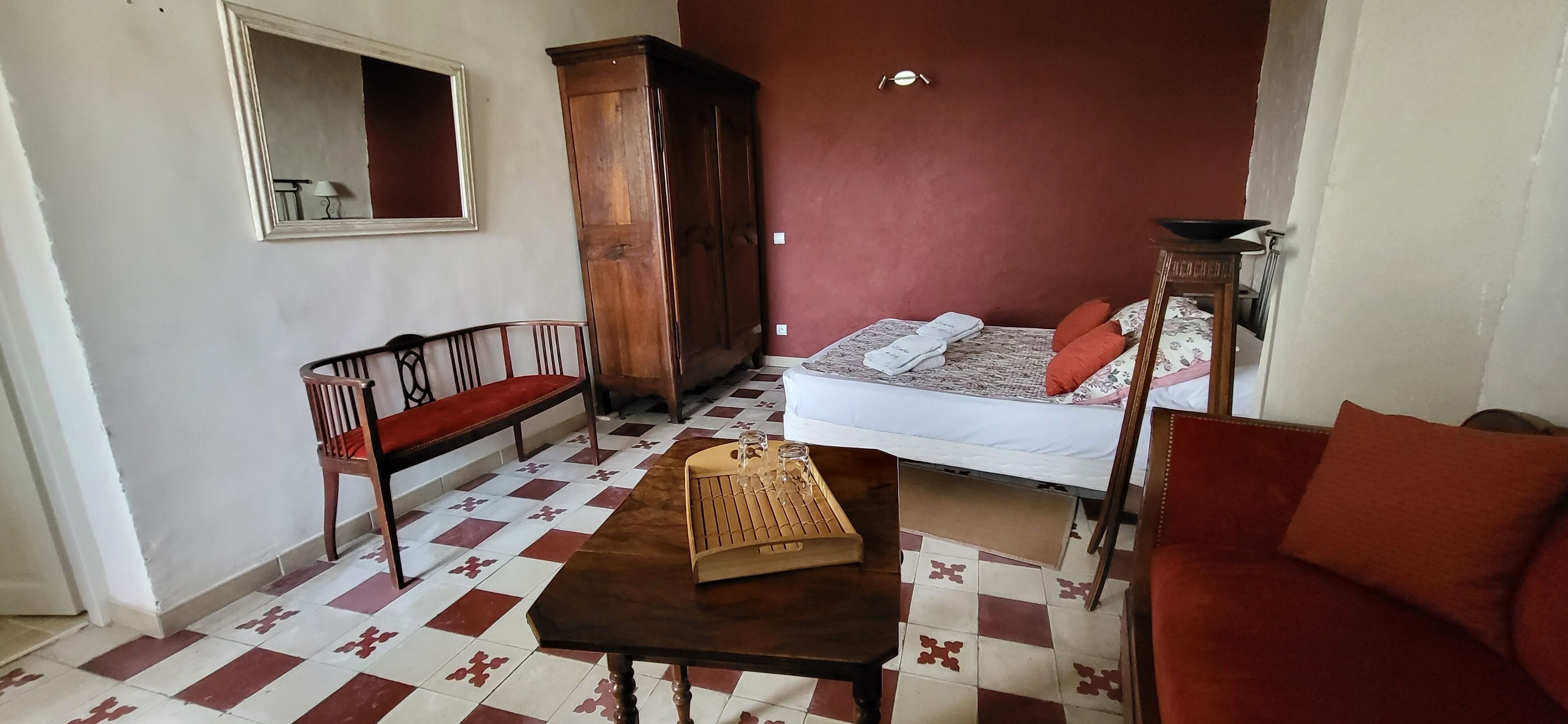 Een kamer met een geruite vloer, een houten bank, een bed met rode kussens, een houten kast en een tafel met dienblad.
