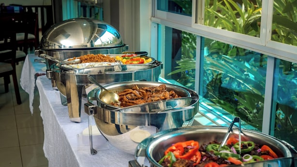 Una mesa de buffet con diversos alimentos, una ventana con vistas a zonas verdes y un mantel blanco.