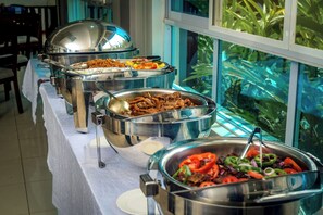 Una taula de buffet amb diferents aliments, una finestra que dona a vistes de vegetació i un mantell blanc.