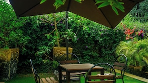 Un patio con una mesa y sillas bajo una sombrilla, rodeado de exuberante follaje y plantas en flor.