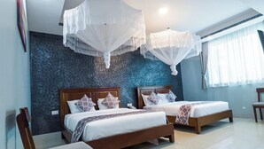 Habitación de hotel con dos camas, una silla y un ventanal con cortinas.