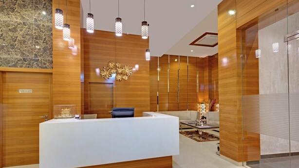 Un área de recepción moderna con un mostrador central blanco, paneles de madera y una lámpara decorativa.