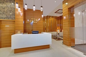 Un espace d’accueil moderne avec un comptoir de réception central blanc, un lambris en bois et un lustre décoratif.