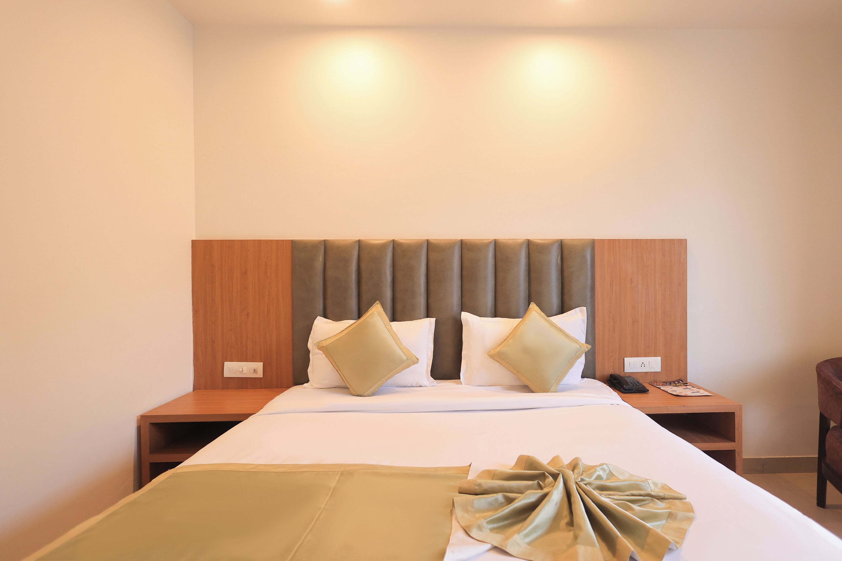 A hotel room with a large bed, a wooden headboard, two bedside tables, and a chair.