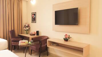 A hotel room with a bed, a desk with a chair, a TV mounted on the wall, and a small table with a vase of flowers.