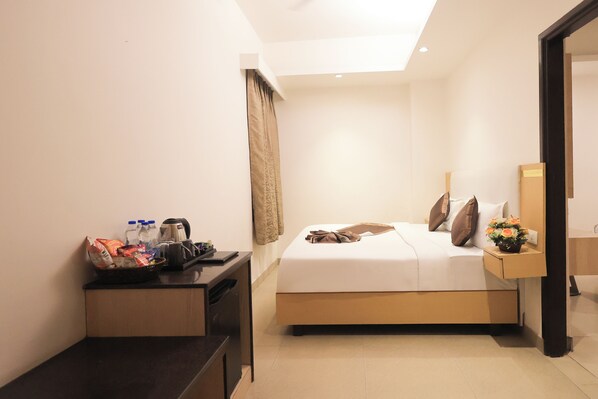 Quarto de hotel com uma cama, mesa de cabeceira e pequena escrivaninha com uma cesta de objetos.