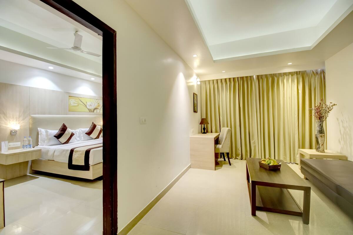 Una habitación de hotel moderna con cama, mesita de noche, lámpara y vista al área de estar.