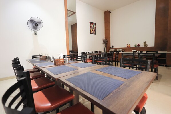 A dining area with multiple tables and chairs, a standing fan, and a decorative wall piece. - ECKO Lite MARS Hotel, Amritsar (Amritsar)