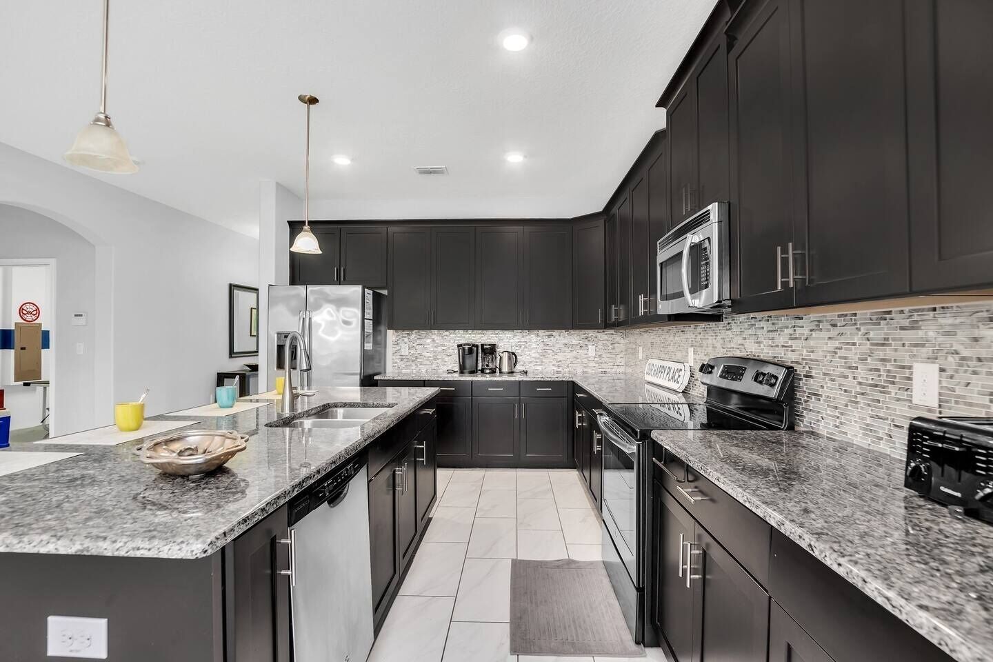 A modern kitchen with dark cabinetry, a granite countertop, stainless steel appliances, and a brick backsplash.