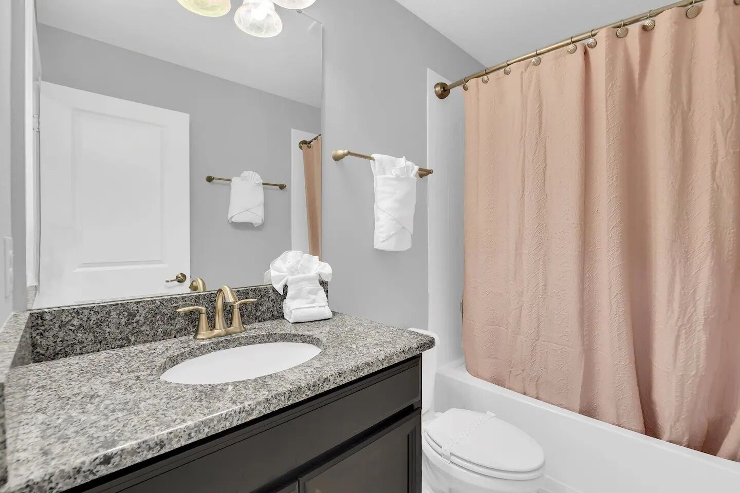 Une salle de bain avec un lavabo surmonté d’un plan de travail en granit, des toilettes blanches et un rideau de douche beige.
