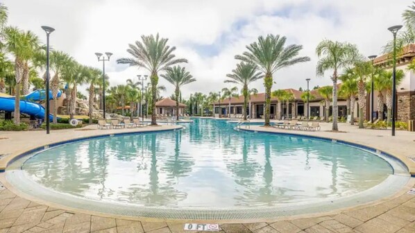 A large outdoor swimming pool with a surrounding patio area, palm trees, and a blue slide. - Perfect Disney Vacation! Waterpark, Lazyriver! (Davenport)