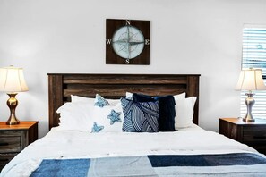 Una cama bien tendida con sábanas blancas y detalles azules, un cabecero de madera y una decoración de brújula en la pared.