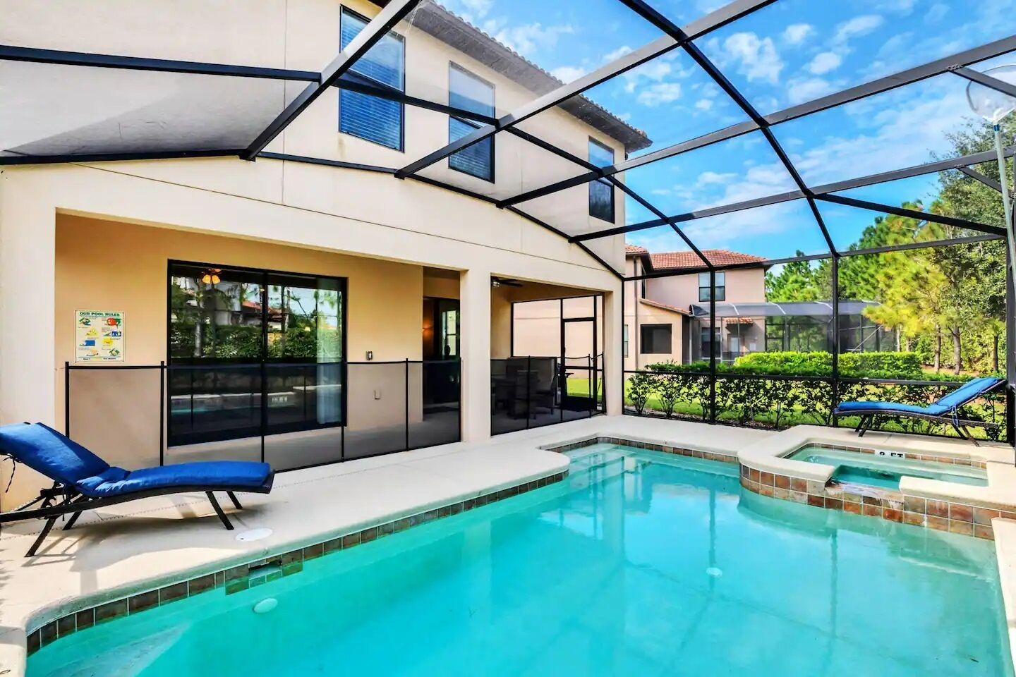 A swimming pool with a glass enclosure, lounge chairs, and a view of neighboring houses.