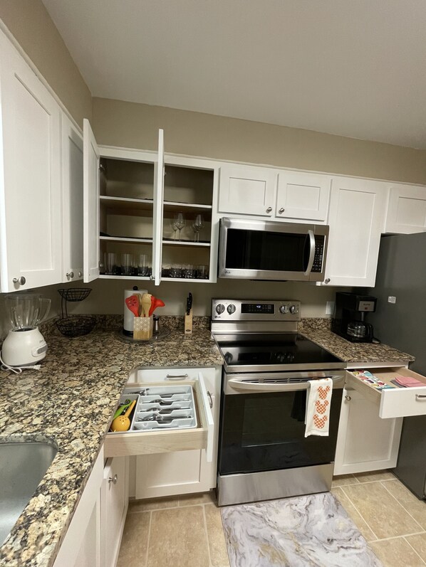 A kitchen with white cabinets, a microwave, an oven, and a granite countertop.