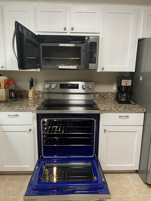 Uma cozinha com armários brancos, micro-ondas preto, forno de aço inoxidável e cafeteira.
