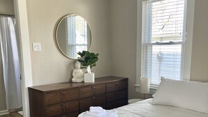 Une chambre avec un grand lit, une commode, un miroir et une fenêtre avec des stores.