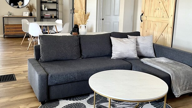 Un salon moderne avec un canapé gris, une table basse ronde et un grand miroir.