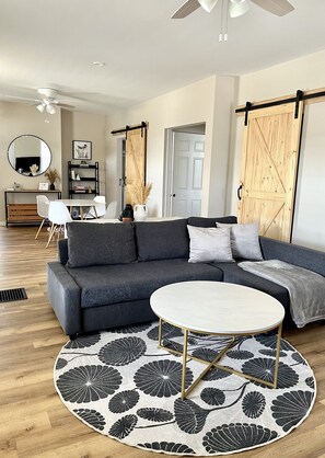 A modern living room with a grey sofa, a round coffee table, and a large mirror. - Rest & Recharge in Findlay, OH (Findlay)