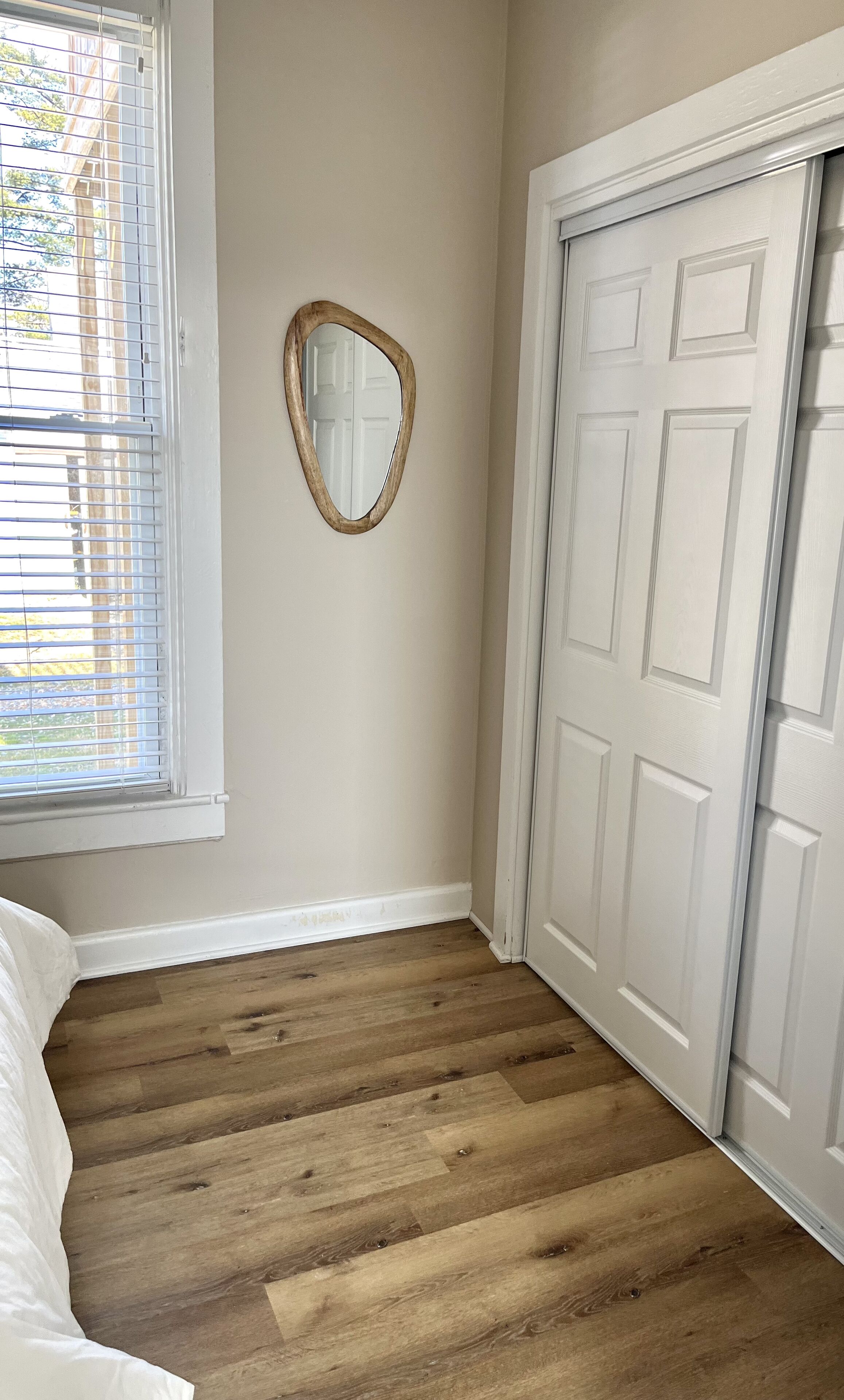 A room with a wooden floor, a white door, and a window with blinds.
