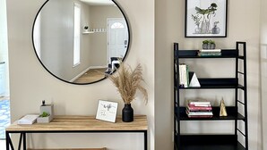 Une pièce comprenant une console en bois, une étagère en métal noir, un miroir et un tableau encadré accroché au mur.