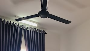 Een hotelkamer met een bed, gordijnen, een plafondventilator en een raam.