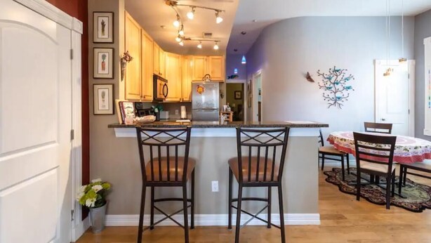 A kitchen with wooden cabinets, a central island with two chairs, and a dining area with a table and chairs. - Private Condo in heart of downtown Golden, CO. (Golden)