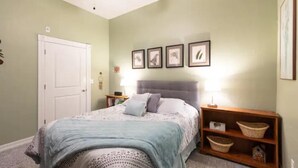A bedroom with a bed, a nightstand, a wooden shelf with baskets, and framed pictures on the wall. - Private Condo in heart of downtown Golden, CO. (Golden)