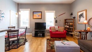 A living room with a red sofa, a television, a bookshelf, and a dining area with chairs and a table. - Private Condo in heart of downtown Golden, CO. (Golden)