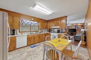 Une cuisine compacte avec des meubles en bois, un four encastré et un coin repas comprenant une table jaune et des chaises blanches.