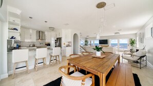 Une cuisine moderne avec des meubles blancs, une table à manger en bois et une vue sur l’océan.