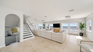 Un vaste espace de vie comprenant un grand canapé blanc, un téléviseur à écran plat et un escalier menant à un niveau supérieur.